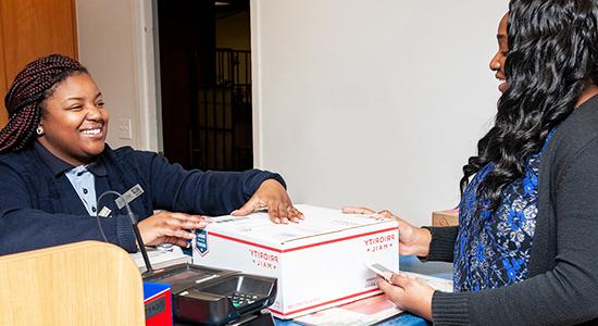 人们在邮局柜台将优先邮件包裹交给美国邮政总局的零售助理.